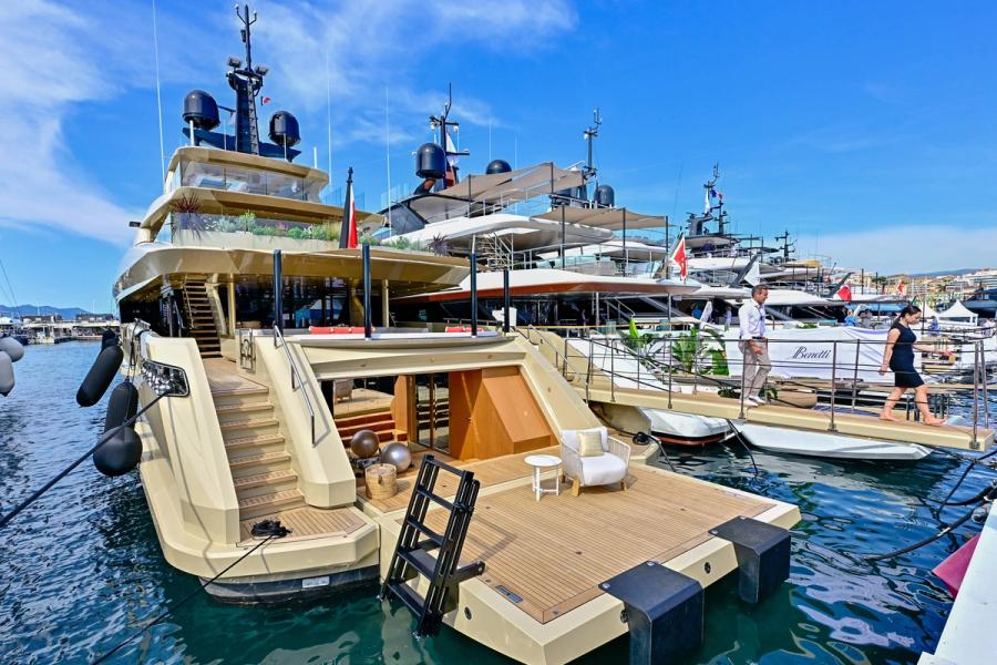 Luxury yacht docked at a marina with calm waters and a clear sky.