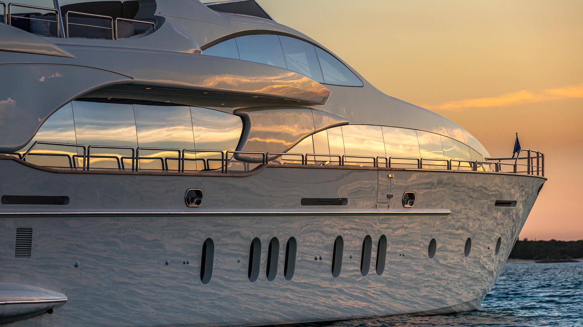 Side view of a sleek luxury yacht docked at sunset with golden reflections on water