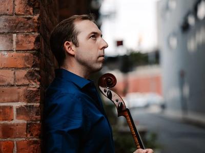 Brook Speltz against a brick wall, cello scroll in profile