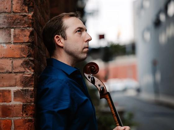 Brook Speltz against a brick wall, cello scroll in profile