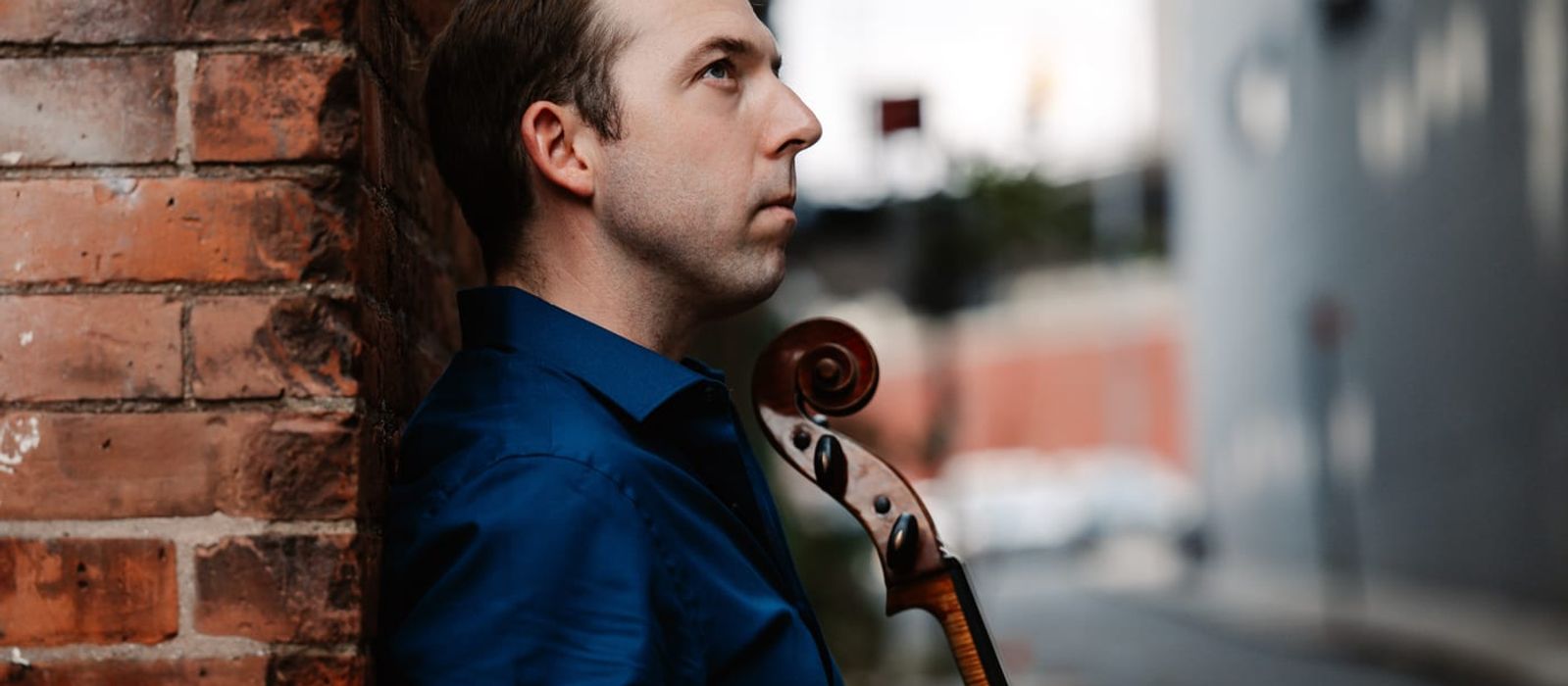 Brook Speltz against a brick wall, cello scroll in profile