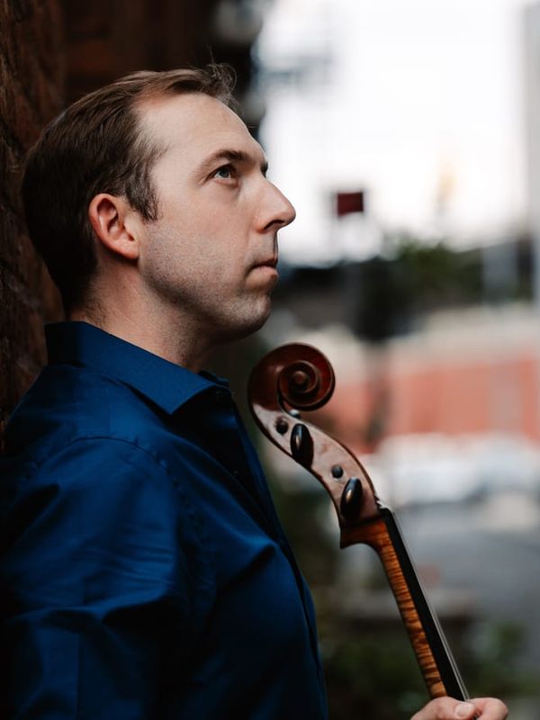 Brook Speltz against a brick wall, cello scroll in profile