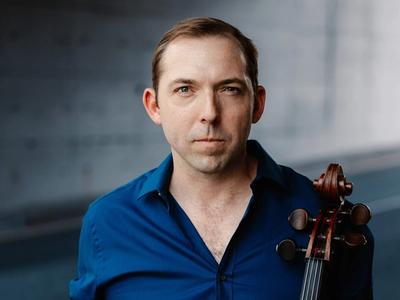 Brook Speltz in a parking garage, blue shirt, with cello
