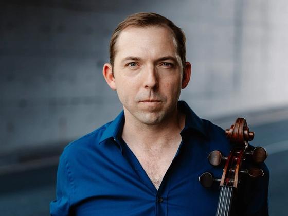Brook Speltz in a parking garage, blue shirt, with cello