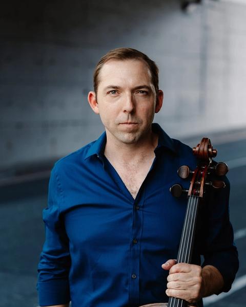 Brook Speltz in a parking garage, blue shirt, with cello