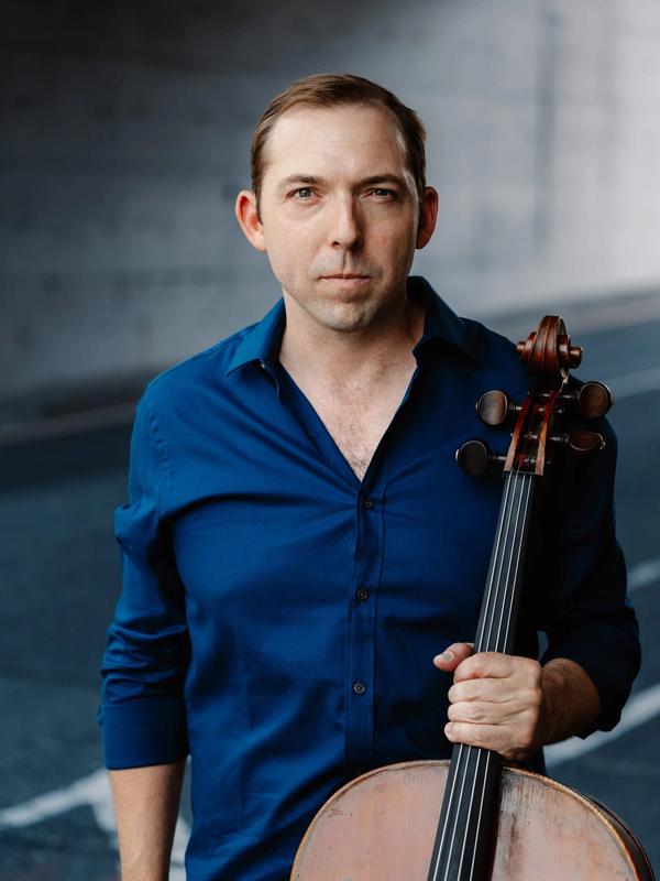 Brook Speltz in a parking garage, blue shirt, with cello