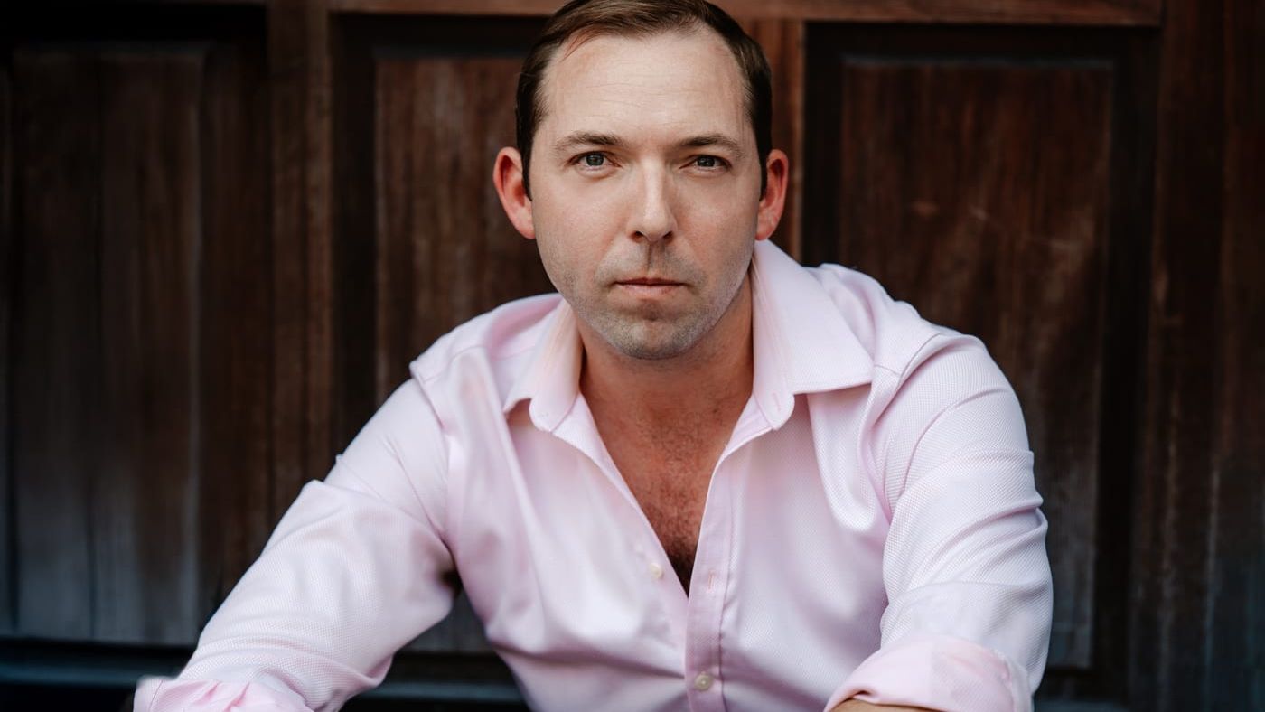 Brook Speltz leaning forward, direct gaze against a dark wood door