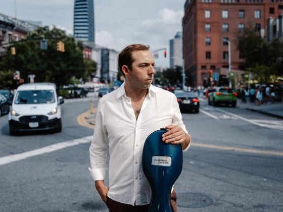 Brook Speltz on a New York City street, white shirt, with cello case
