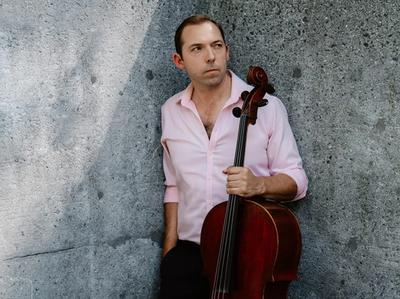 Brook Speltz against a concrete wall, cello held at side
