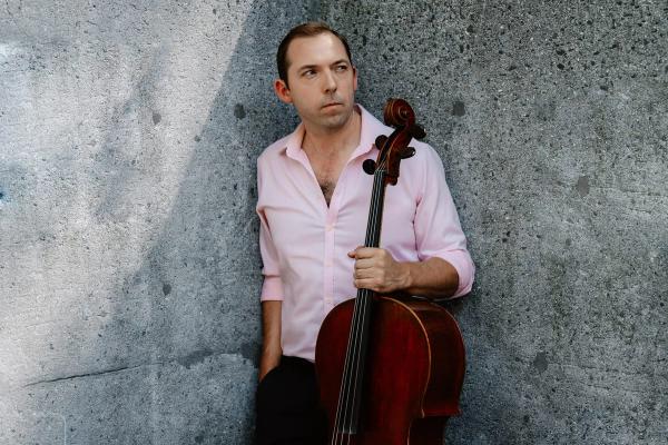 Brook Speltz against a concrete wall, cello held at side