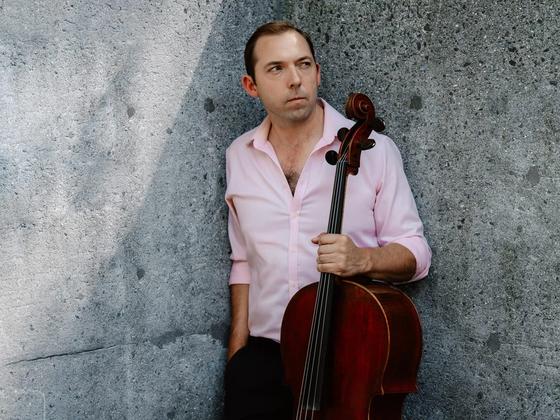 Brook Speltz against a concrete wall, cello held at side