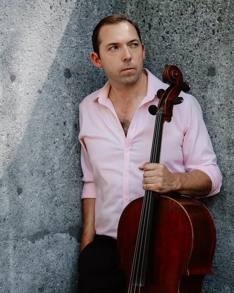 Brook Speltz against a concrete wall, cello held at side