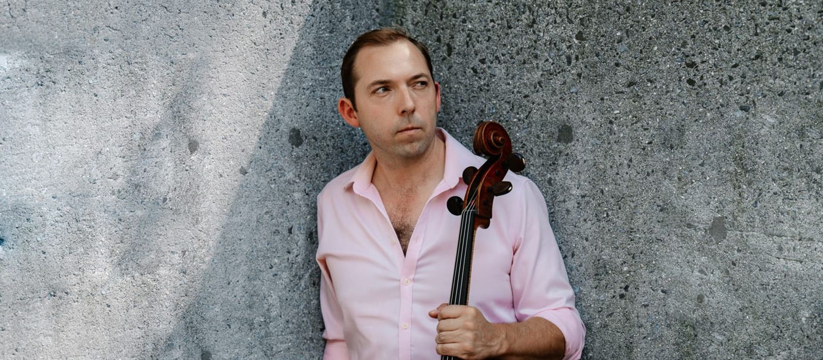 Brook Speltz against a concrete wall, cello held at side