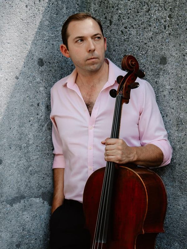 Brook Speltz against a concrete wall, cello held at side