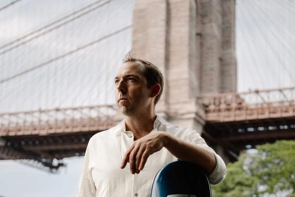 Brook Speltz at the Brooklyn Bridge with cello case, looking up
