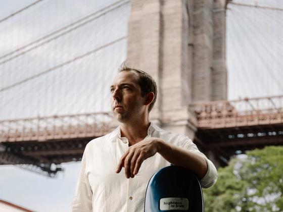 Brook Speltz at the Brooklyn Bridge with cello case, looking up