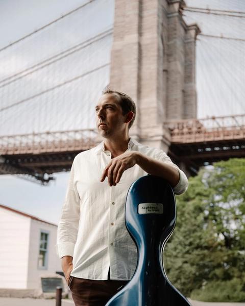 Brook Speltz at the Brooklyn Bridge with cello case, looking up