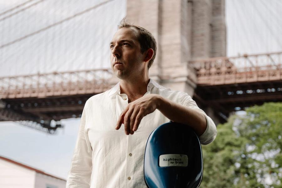 Brook Speltz at Brooklyn Bridge with cello case, looking up