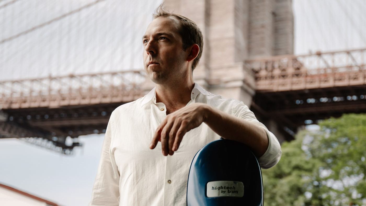 Brook Speltz at Brooklyn Bridge with cello case, looking up