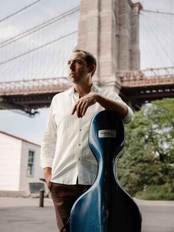 Brook Speltz at the Brooklyn Bridge with cello case, looking up