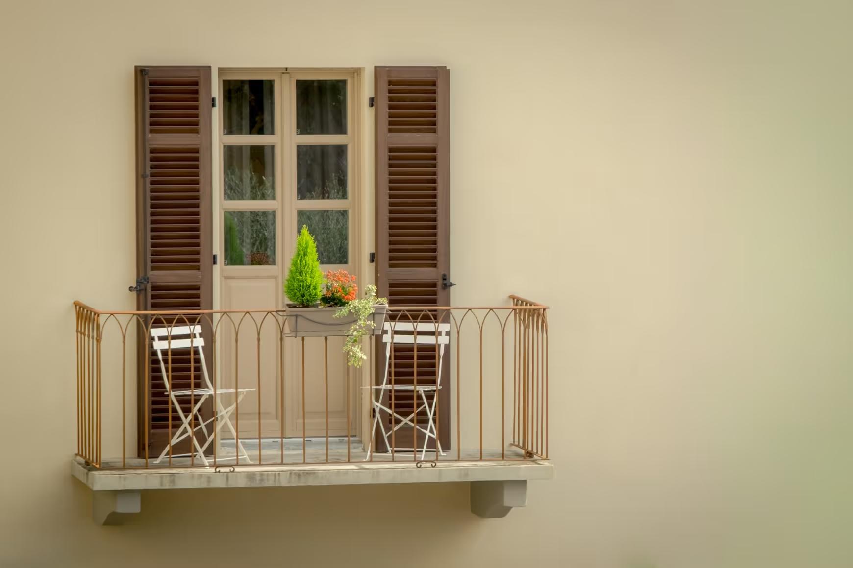 Small balcony with two chairs and a flower box in front of a shuttered door