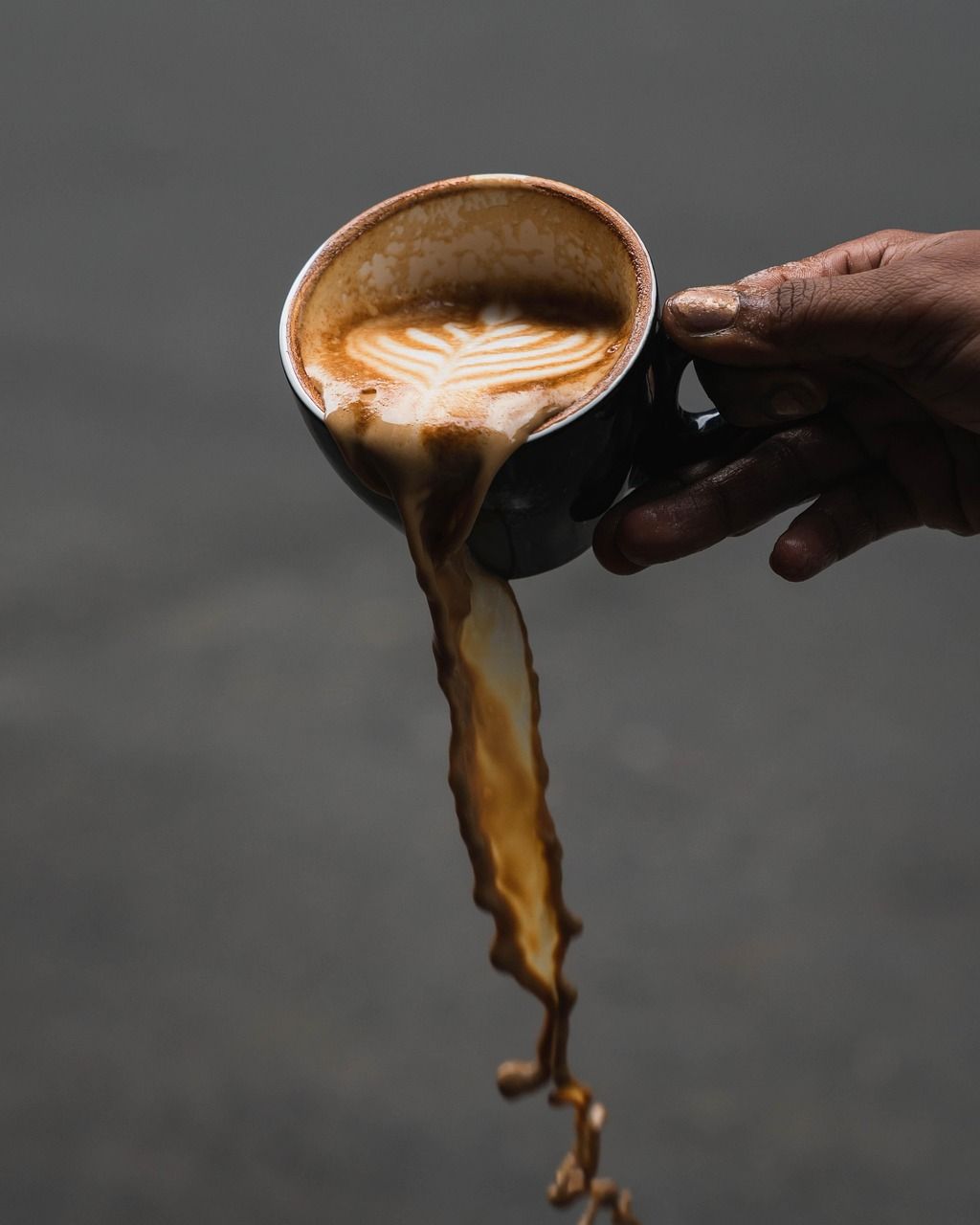 Une main tient une tasse dont le café déborde