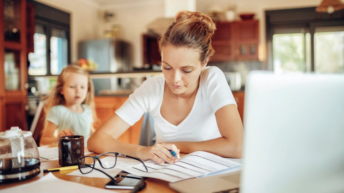 Military spouse managing household tasks with young child in kitchen background