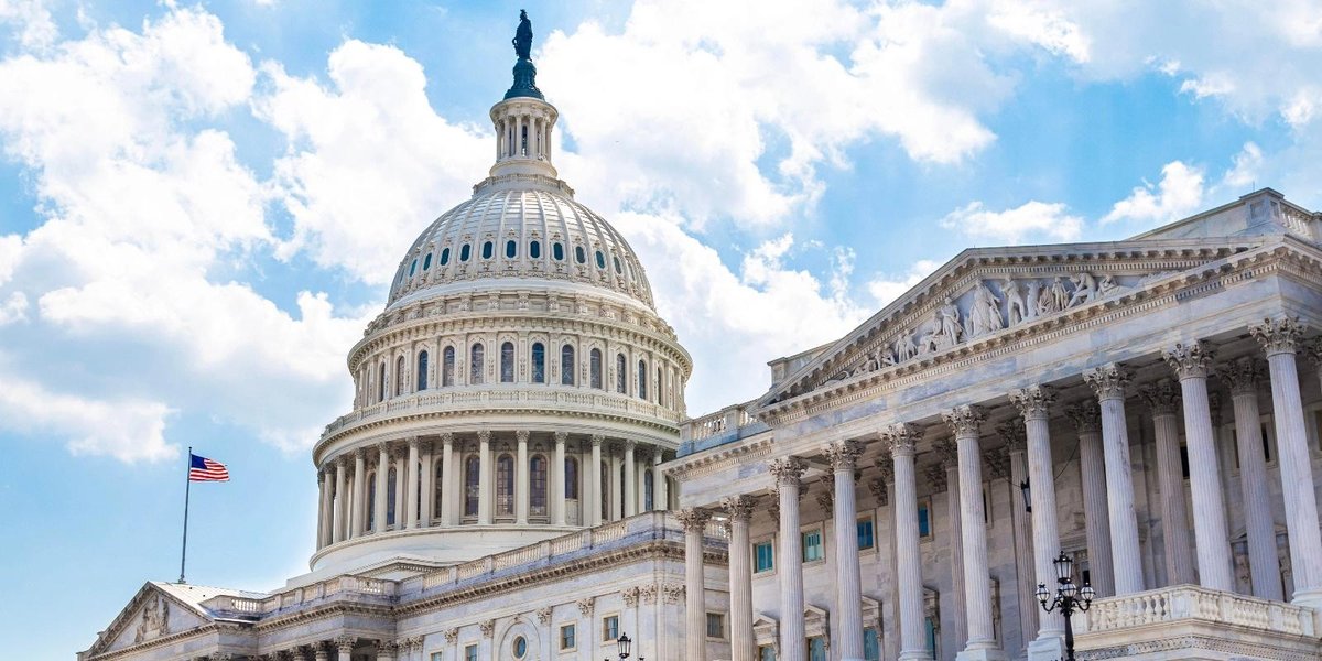 U.S. Capitol building exterior with American flag, under blue sky with clouds