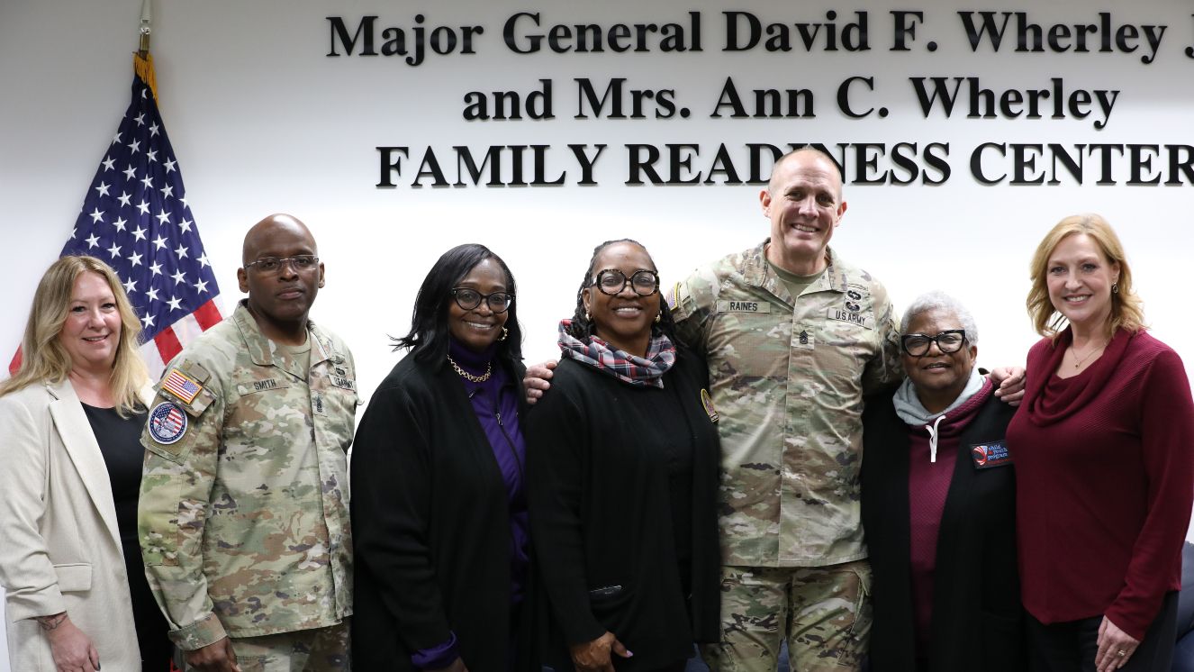 Seven individuals stand together for a group photo taken during their visit to the Family Readiness Support team.