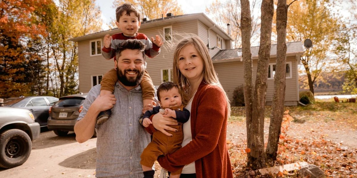 Military family smiling outside home in autumn, with trees and parked cars in background