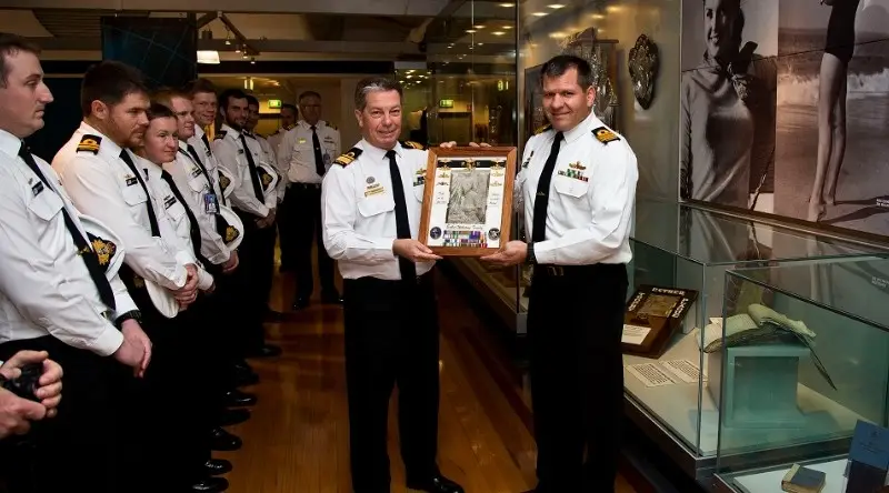 Two captains hold a picture of Esther Williams as a row of seamen look on.