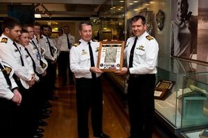 Two captains hold a picture of Esther Williams as a row of seamen look on.