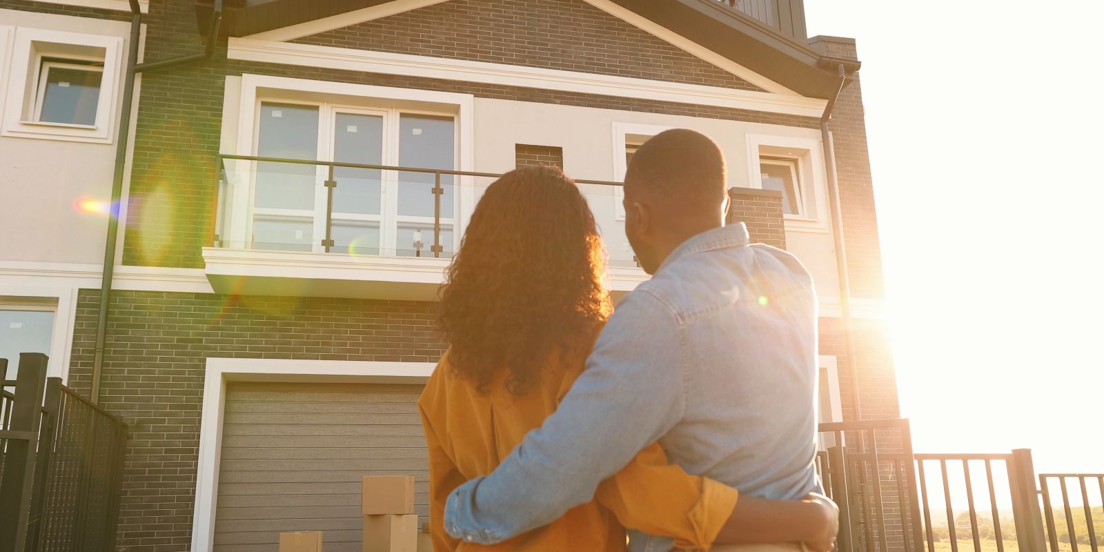 A young just-married couple standing at yard of house, hugging and observing second floor.