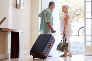 Older couple leaves a house with luggage.