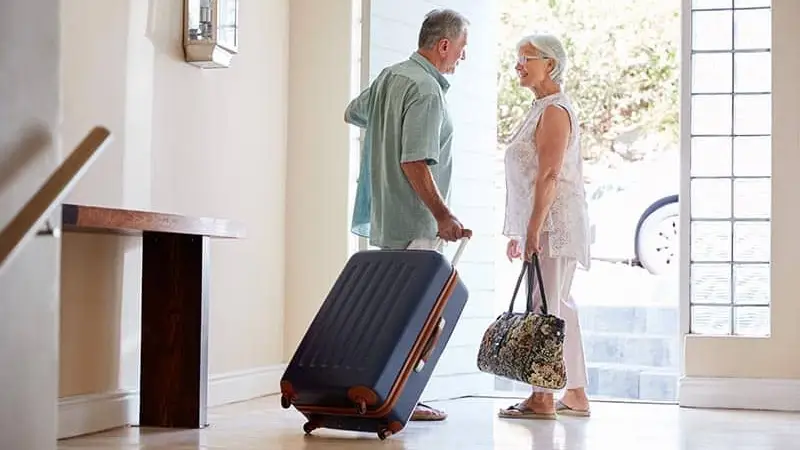 Older couple leaves a house with luggage.