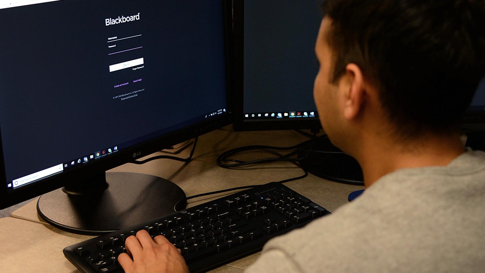 A soldier sits in front of a computer, “Blackboard Learning” Software on the screen.