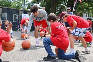 A young adult plays basketball with a group of young boys.