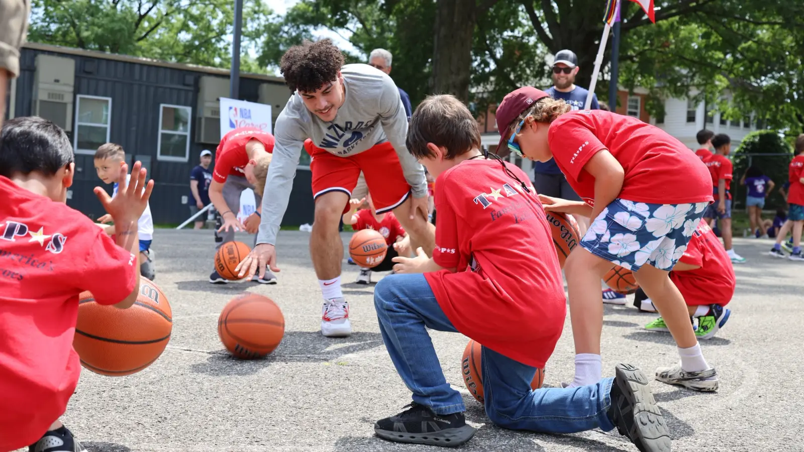 A young adult plays basketball with a group of young boys.
