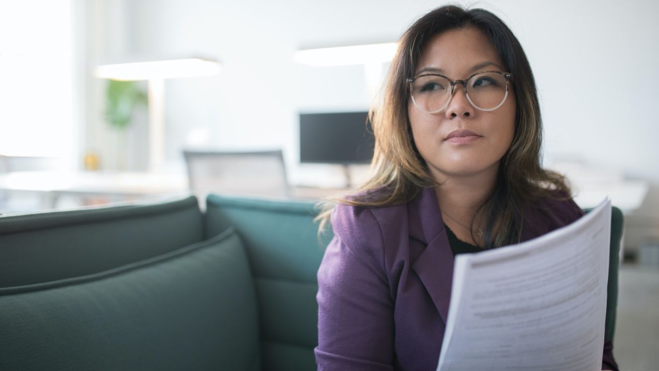 A woman sitting in an office holding a paper looking in the distance.