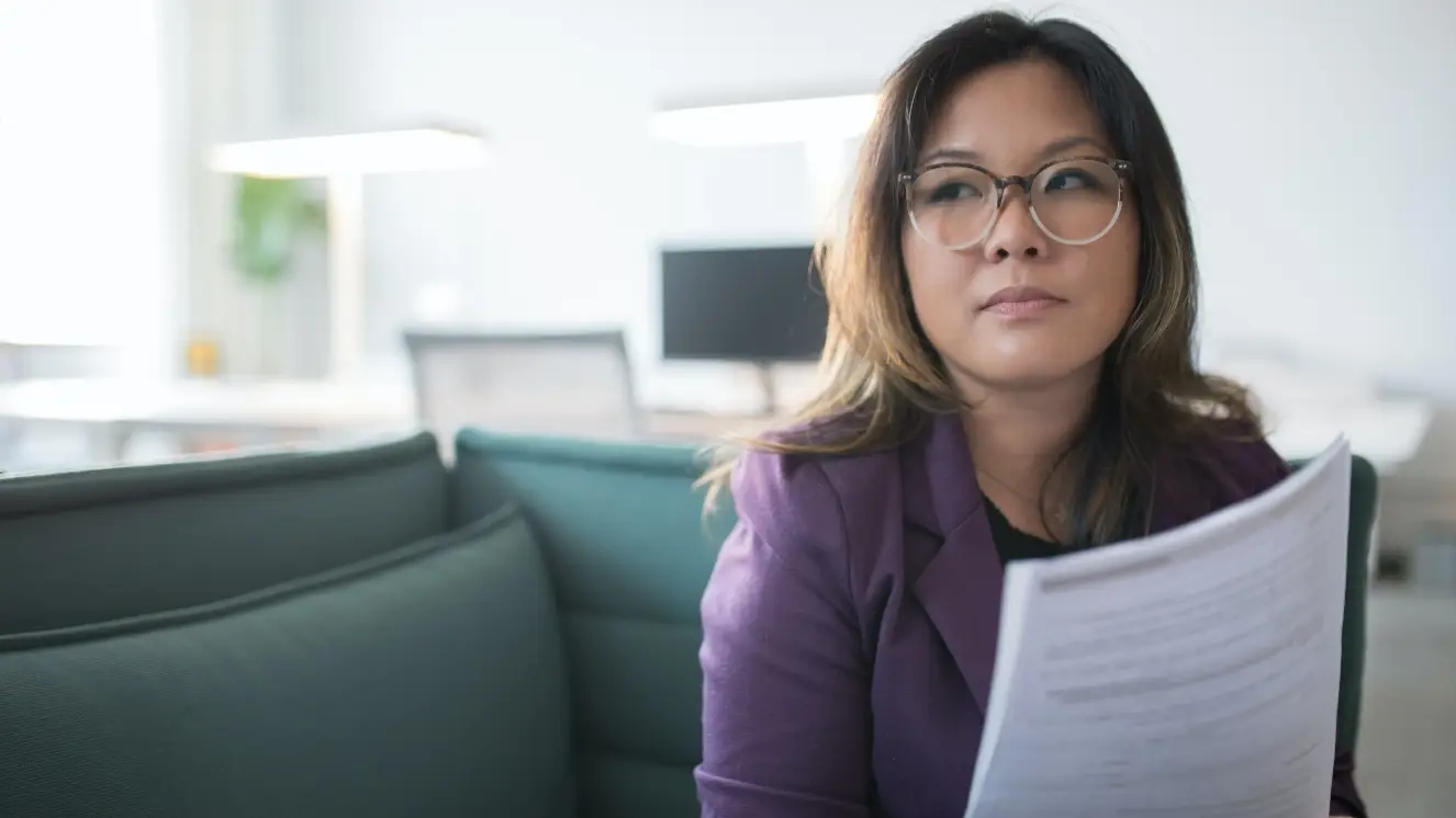 A woman sitting in an office holding a paper looking in the distance.