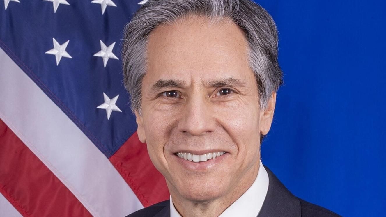 Secretary of State Antony Blinken in front of an American flag backdrop.