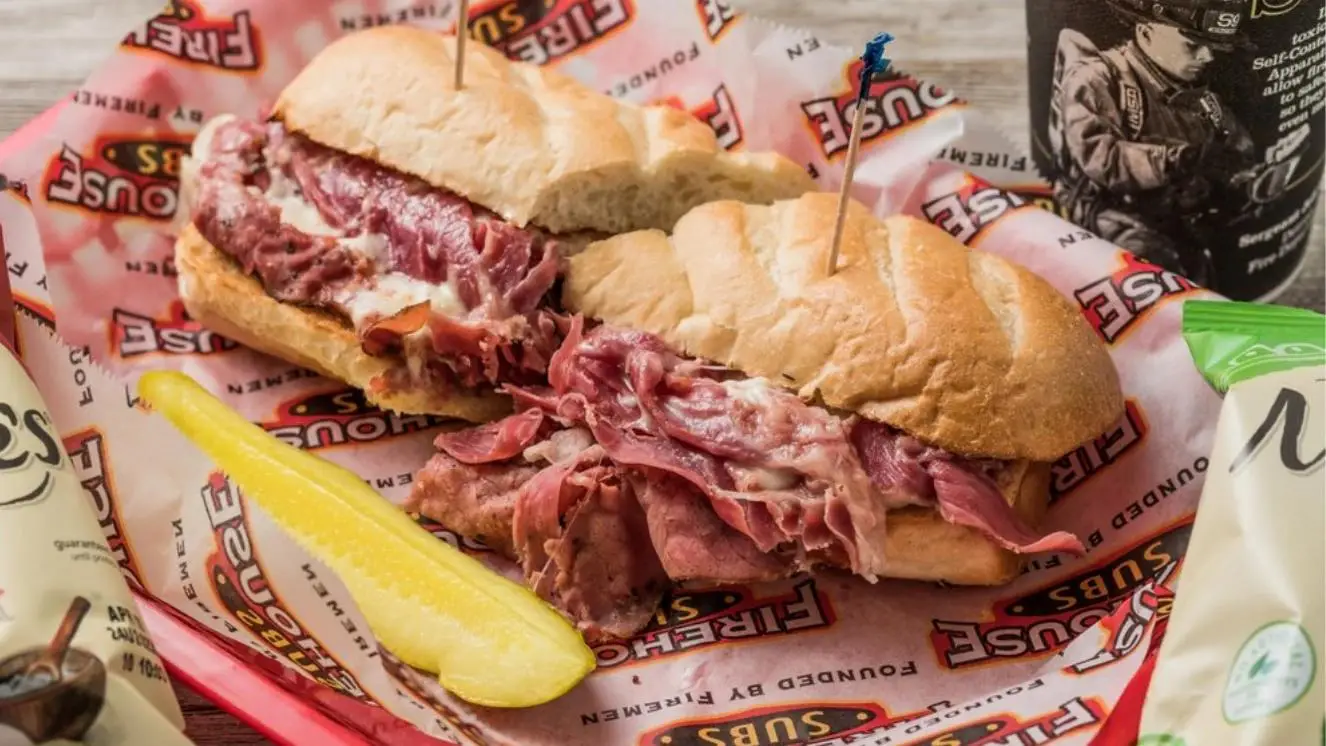 Firehouse Subs sandwich with pickle spear and chips on branded wrapper.