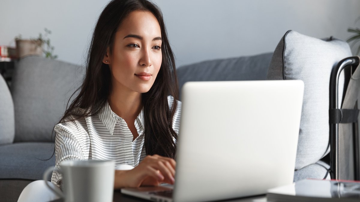 A woman smiles as she reads a laptop screen.