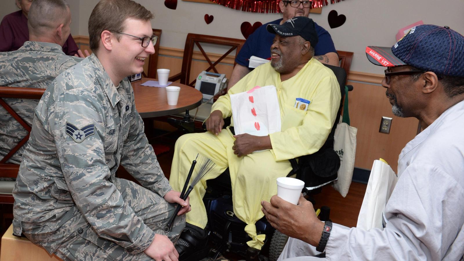 A uniformed man laughs and talks to two veterans in wheelchairs.