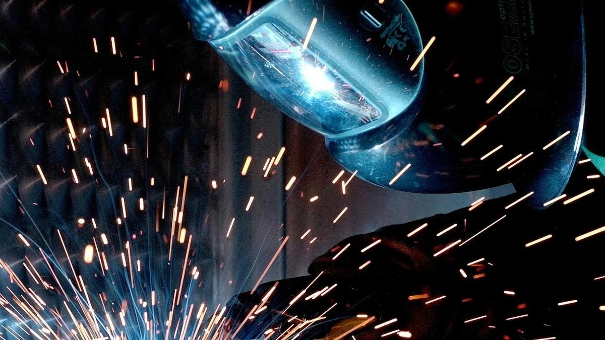 Welder wearing protective gear with sparks flying in workshop.