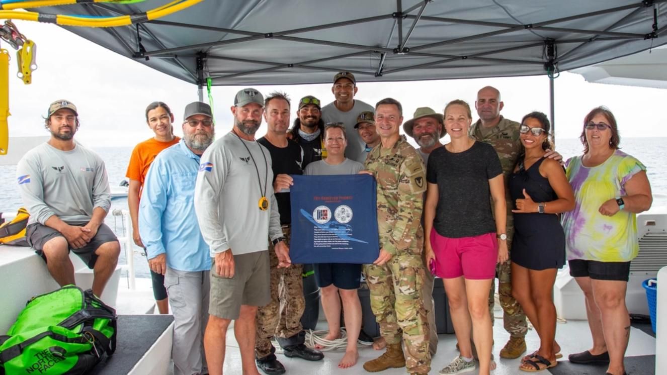 Project Recover team and military personnel on boat holding commemorative plaque at sea