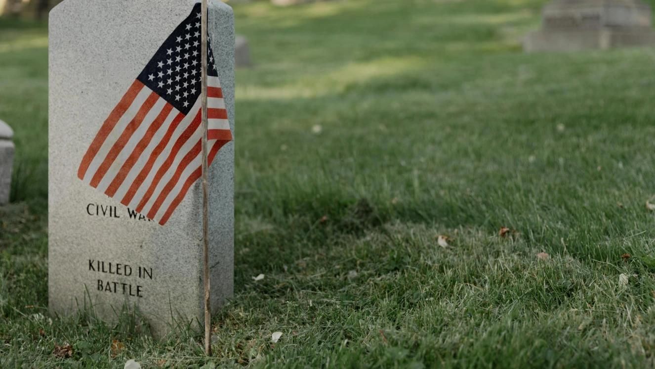 Civil War gravestone with American flag in grassy cemetery.
