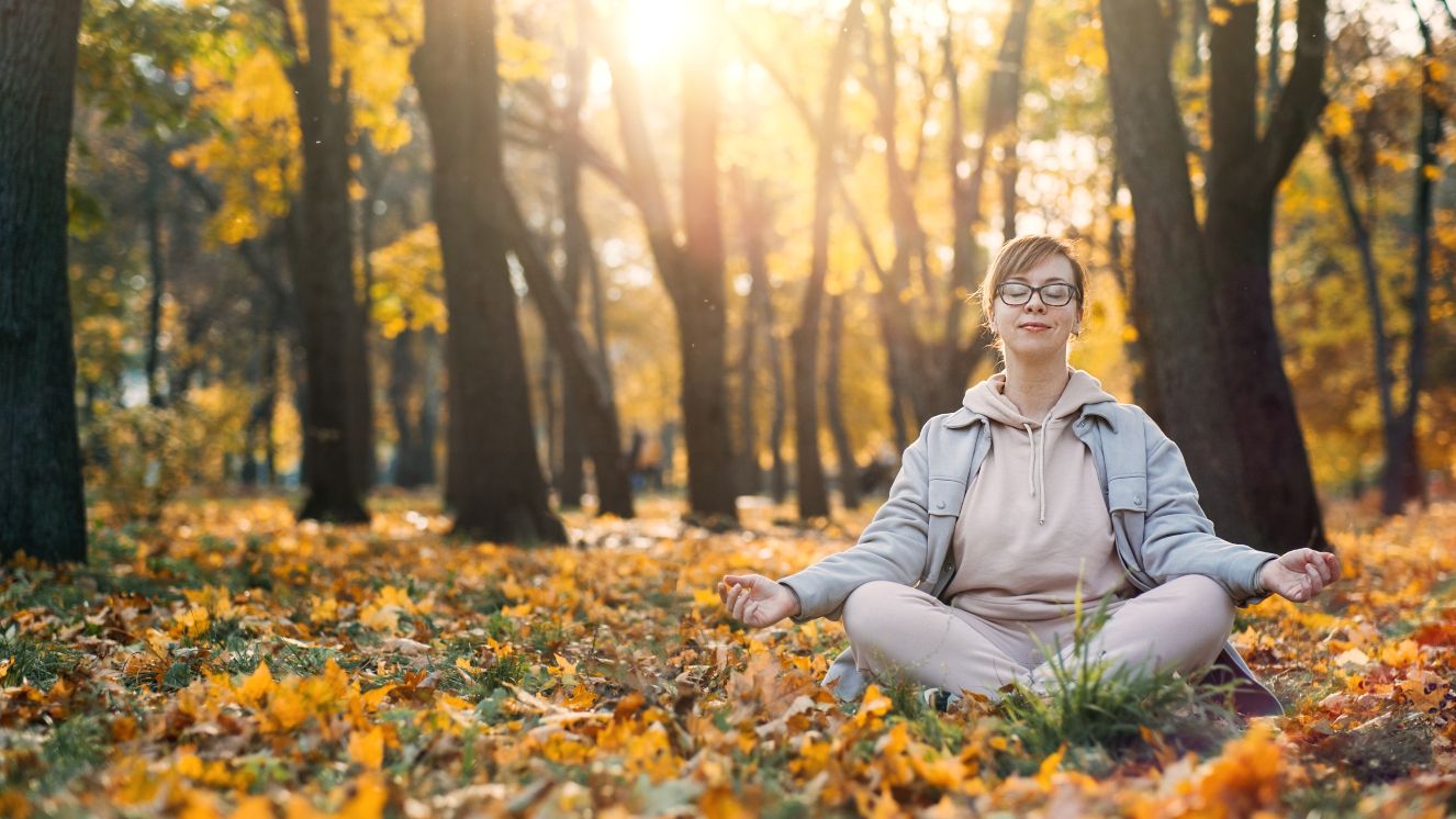 A milspouse meditating in a lotus pose at a park with sunlight in the background.