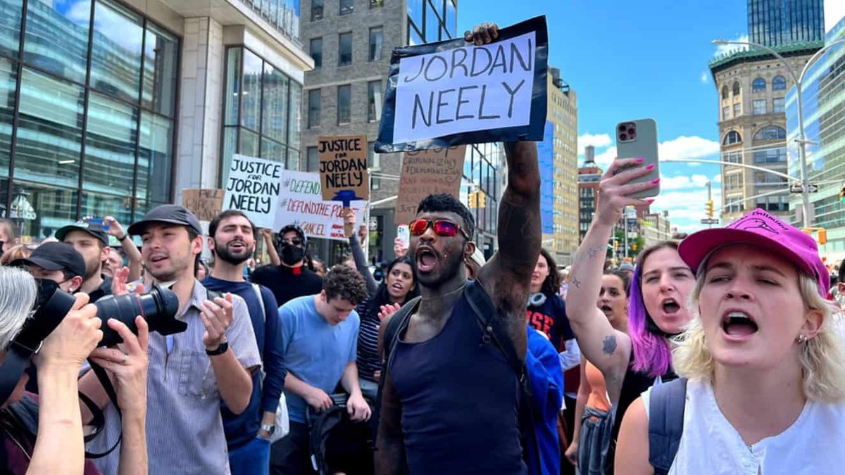 Protesters in NYC holding "Justice for Jordan Neely" signs on busy street.