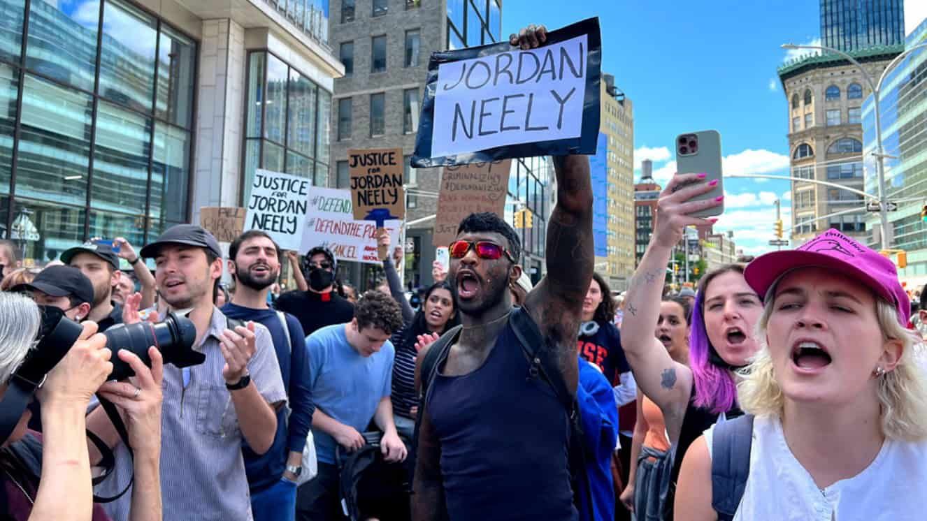 Protesters in NYC holding "Justice for Jordan Neely" signs on busy street.